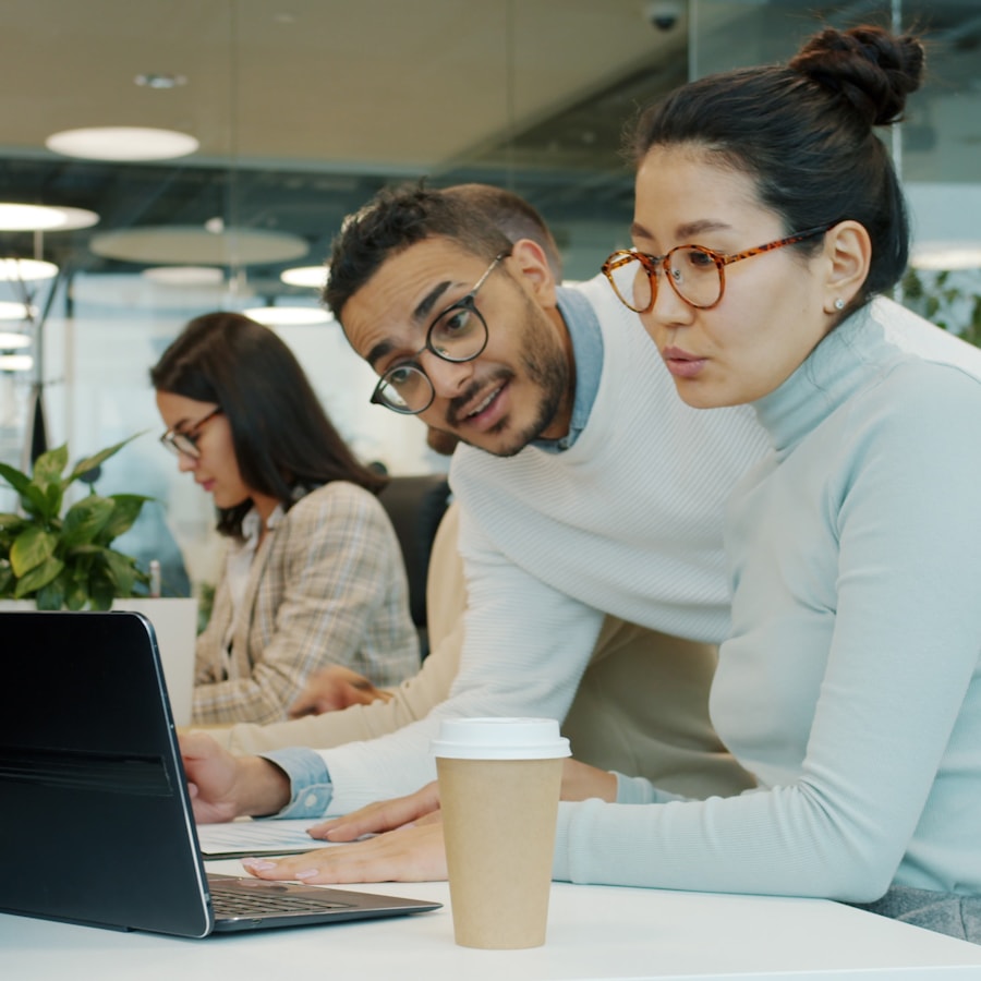 Dua profesional berkolaborasi erat di atas laptop dalam kantor yang cerah dan modern.