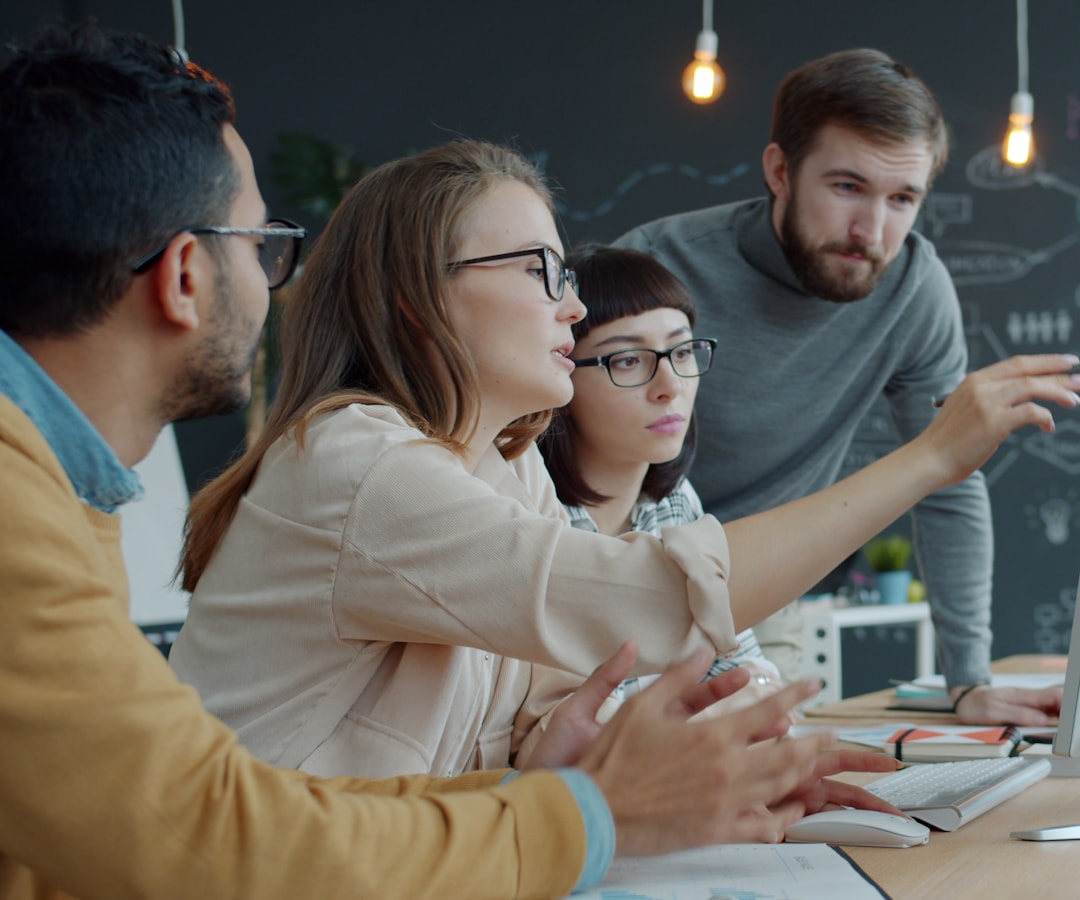 A small team gathered around a laptop, pointing at the screen during a product discussion.